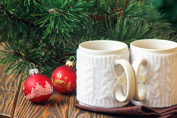 Christmas Decoration with fir twigs, red balls, marshmallow and cups of hot chocolate dressed in knitted warm winter mug holder on wooden background
