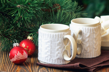 Christmas Decoration with fir twigs, red balls, marshmallow and cups of hot chocolate dressed in knitted warm winter mug holder on wooden background