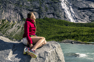 Naklejka na ściany i meble Young woman is sitting on the stone, Briksdalsbreen, Norway