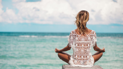 young woman meditation in a yoga pose at the beach