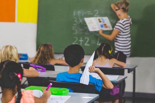 Boy with a paper plane while teacher teaching in classroom