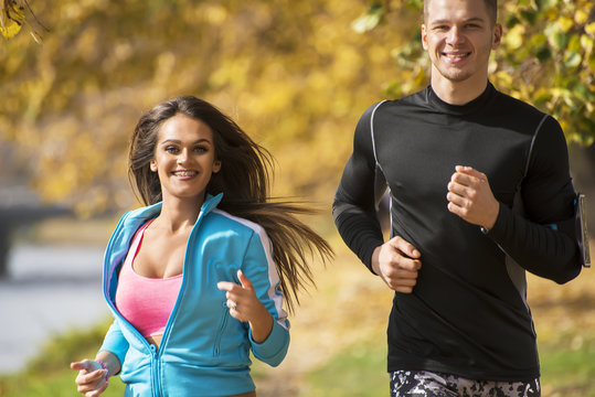 Beautiful young couple running together in the park. Autumn environment.
