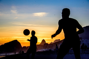 Beautiful sunset and silhouettes of men playing dar toques na bola game at Copacabana beach, Rio de Janeiro, Brazil