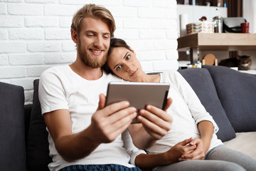 Beautiful couple looking at tablet smiling sitting on sofa  home.
