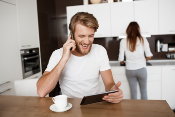 Man looking at tablet talking on phone smiling. Girlfriend background.