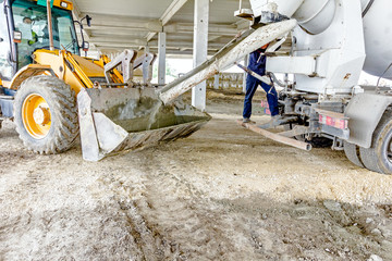 Workers are unloading concrete with shovel from excavator's fron