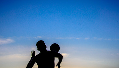 The silhouette of a jumping man playing the ball on the background of blue sky at sunset time on...