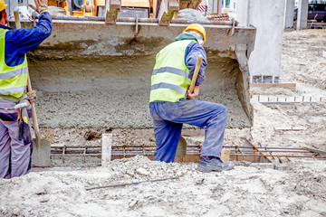 Workers are unloading concrete with shovel from excavator's fron