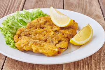Weiner schnitzel with green salad and lemon on a wooden background