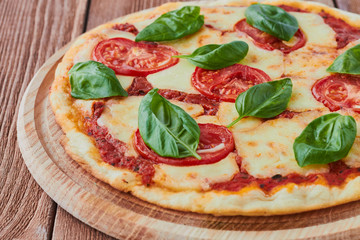 Pizza Margherita with tomatoes, mozzarella and basil on a wooden background сlose up.