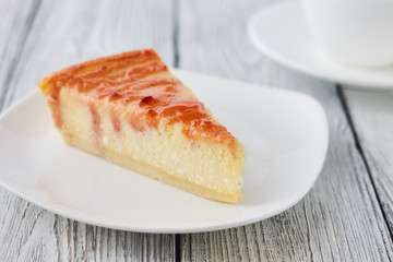 Slice of the New York cheesecake on a white plate on a wooden background
