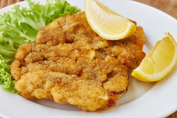 Weiner schnitzel with green salad and lemon on a wooden background