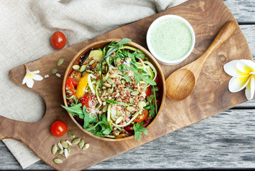 Salad with quinoa, zucchini and arugula in wooden bowl on the wooden board. View from above