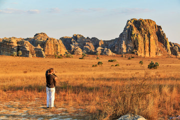 Tourist taking photos at sunset near the famous rock formation 'La Fenetre' in Isalo, Madagascar - obrazy, fototapety, plakaty