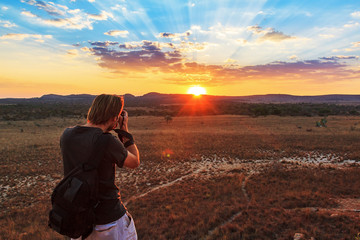 Tourist taking photos at sunset near the famous rock formation 'La Fenetre' in Isalo, Madagascar