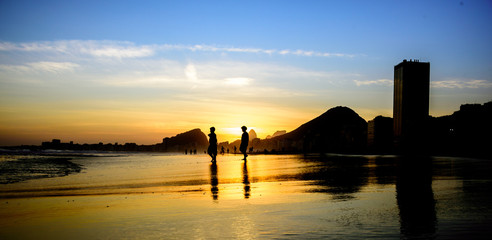 Silhouettes of two boys walking at the edge of Atlantic ocean on the background of the beautiful sunset at Copacabana beach, Rio de Janeiro, Brazil