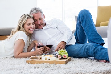 Cheerful couple with red wine and food while lying on rug