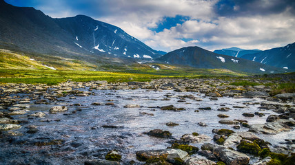 meadow with mountain river in front of Ural mountain ridge