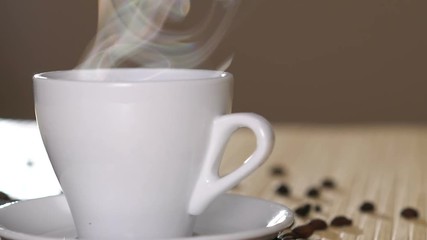 Close up of a white cup of evaporating coffee on table near roasted beans