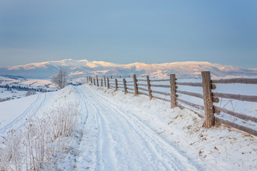 Fototapeta na wymiar Winter country landscape with timber fence and snowy road into evergreen forest