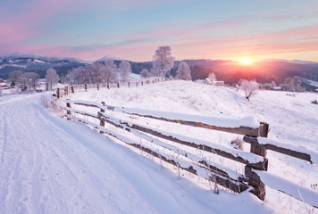 Winter country landscape with timber fence and snowy road into evergreen forest