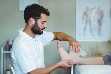 Physiotherapist putting bandage on injured feet of patient