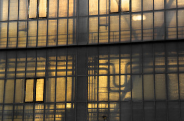 Element of factory architecture - window made from opaque and translucent glass. Silhouette of pipeline inside industrial building. Dramatic yellow / orange backlight