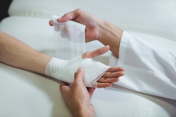 Physiotherapist putting bandage on injured hand of patient