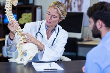 Physiotherapist explaining spine model to patient - Powered by Adobe