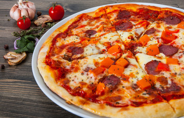 fast food. mexican pizza with pepperoni, vegetables, cheese on wood table