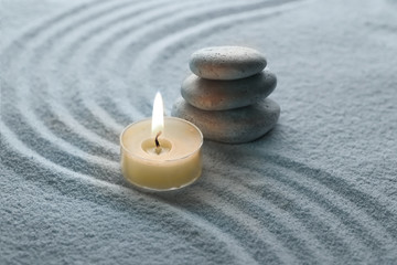 Obraz na płótnie Canvas light warm candle and stone on sand