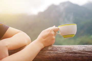 Morning hot drink, coffee or tea cup in female hand on mountain