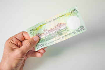 Man holding hundred Bhutanese Ngultrum banknote in his hand