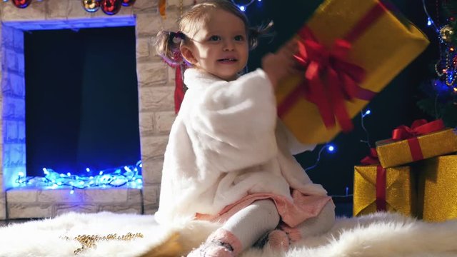 Girl opens Christmas gifts boxes near fireplace, decorated Cristmas tree
