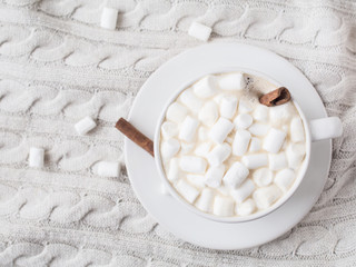 A cup of hot cocoa with Marshmallow and cinnamon sticks on a knitted beige background of Christmas decorations and mandarins, cones. Shallow Selective focus. Copyspace. Top view.