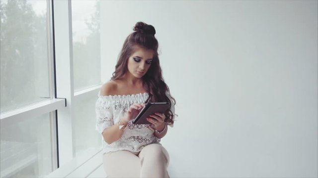 Beautiful woman brunette using her tablet on white background near the window slow motion