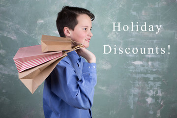 Portrait happy smiling boy teenager with shopping bags on green background and inscription "Holiday Discounts!"