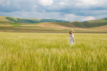 Fototapeta premium Girl in White dress and straw hat walking among fields in countryside