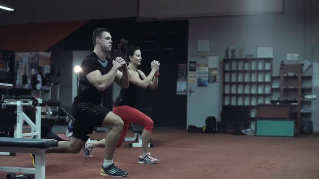 Two fit young athletes doing cardiovascular exercises in a darkened gym in a running motion with raised hands as they work out together in a healthy active lifestyle concept.