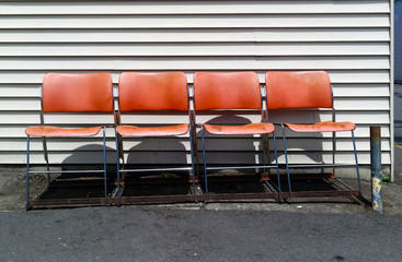 Four faded orange/red chairs against wall. Horizontal.