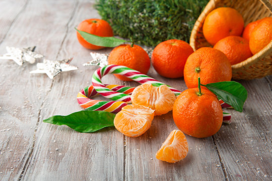 Fresh Tangerines with leaves and Christmas decor with Xmas tree and candies on white old wooden table. Selective focus. Winter holiday concept