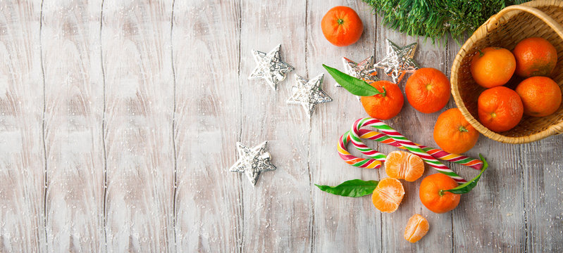 Fresh Tangerines with leaves and Christmas decor with Xmas tree and candies on white old wooden table. Rustic style. Top view. Winter holiday concept, Long web format