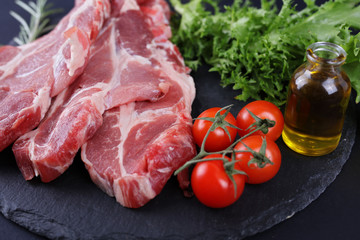 Raw pork neck meat on black background, spices, vegetables, olive oil. Cooking background, healthy eating concept.