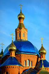 Fototapeta na wymiar The Orthodox Church is of red brick with Golden domes against the blue sky at sunset. Russia, Belgorod. Close-up. Vertical view