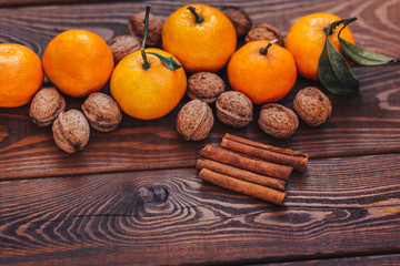 fresh juicy ripe tangerines with leaves walnuts and cinnamon on wood background