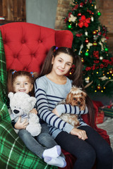 Two girls sit with a dog on the couch. The concept of Christmas