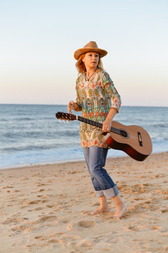 Portrait of a beautiful blond female playing guitar on the beach, sunset sunny blue sky outdoors background
