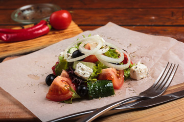 Concept: restaurant menus, healthy eating, homemade, gourmands, gluttony. Greek salad served on paper with ingredients on weathered wooden background.