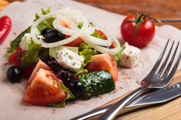 Concept: restaurant menus, healthy eating, homemade, gourmands, gluttony. Greek salad served on paper with ingredients on weathered wooden background.