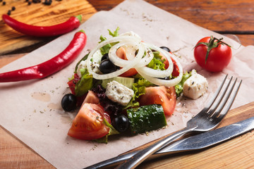 Concept: restaurant menus, healthy eating, homemade, gourmands, gluttony. Greek salad served on paper with ingredients on weathered wooden background.